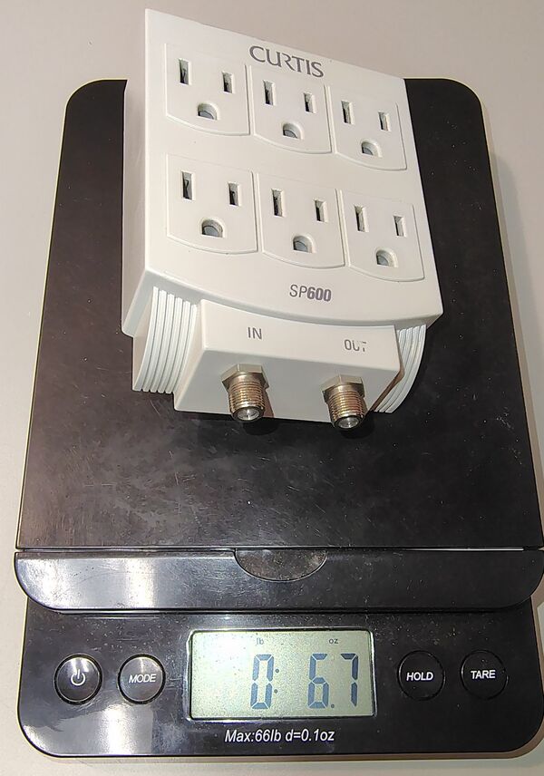 Curtis SP-600 wall-mounted surge protector on a digital scale showing a weight of approximately 6.7 oz (190 g).