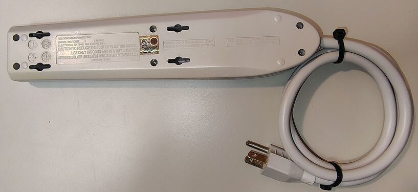 Underside view showing labels, mounting slots, certification markings, enclosure hardware, and attached power cord.