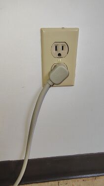 APC-branded right-angle plug installed in a wall receptacle illustrating cord routing.