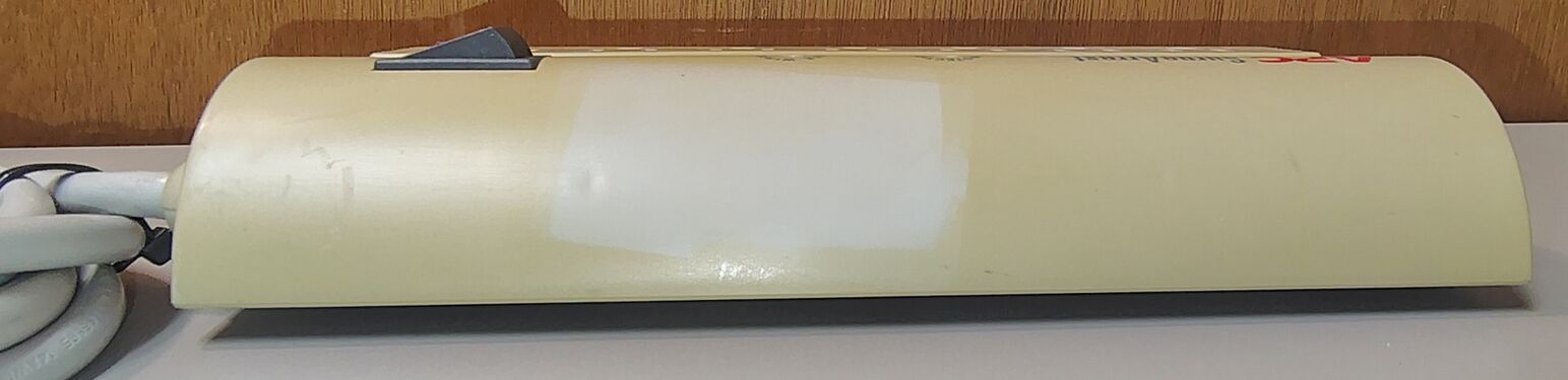 Curved-side profile showing differential enclosure discoloration, including the preserved outline of a previously attached label on the upper housing.