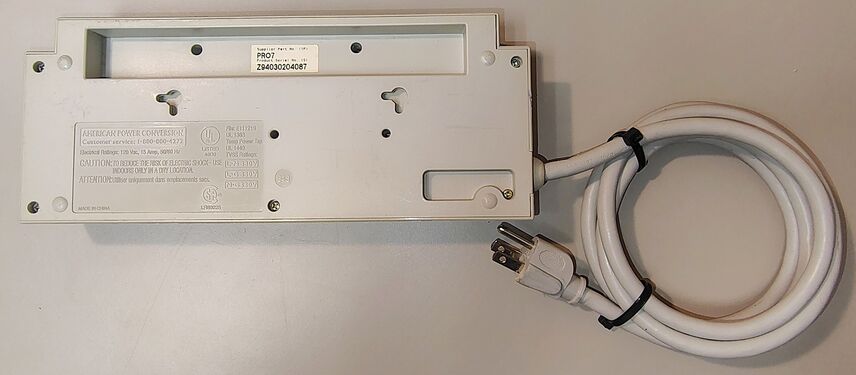 Underside showing product markings, wall-mount slots, enclosure hardware, and attached power cord.