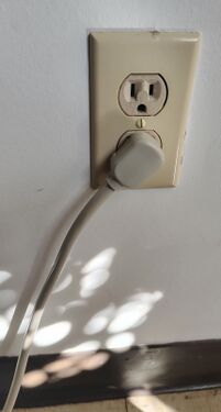 Right-angle plug installed in a wall receptacle illustrating cord routing.