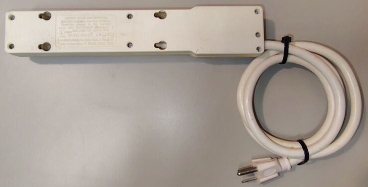 Underside view showing labels, mounting slots, enclosure fasteners, and attached power cord.