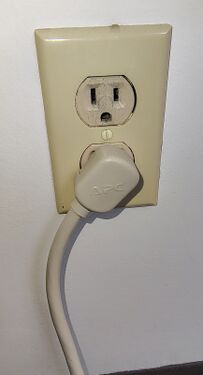 APC-branded right-angle attachment plug installed in a wall receptacle.
