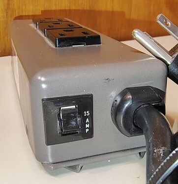 End view showing the heavy-duty power cord, NEMA 5-15P plug, and rounded steel enclosure construction.