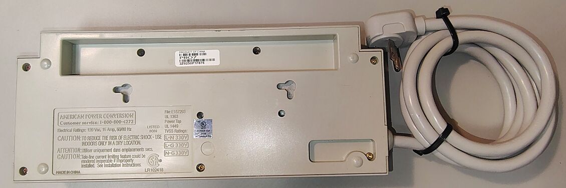 Underside view showing labels, mounting slots, serial-number label, and attached power cord.