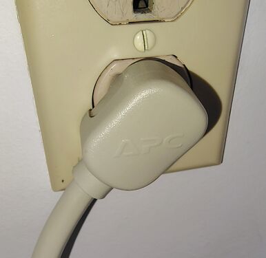 Close-up view of the APC-branded right-angle attachment plug installed in a wall receptacle.
